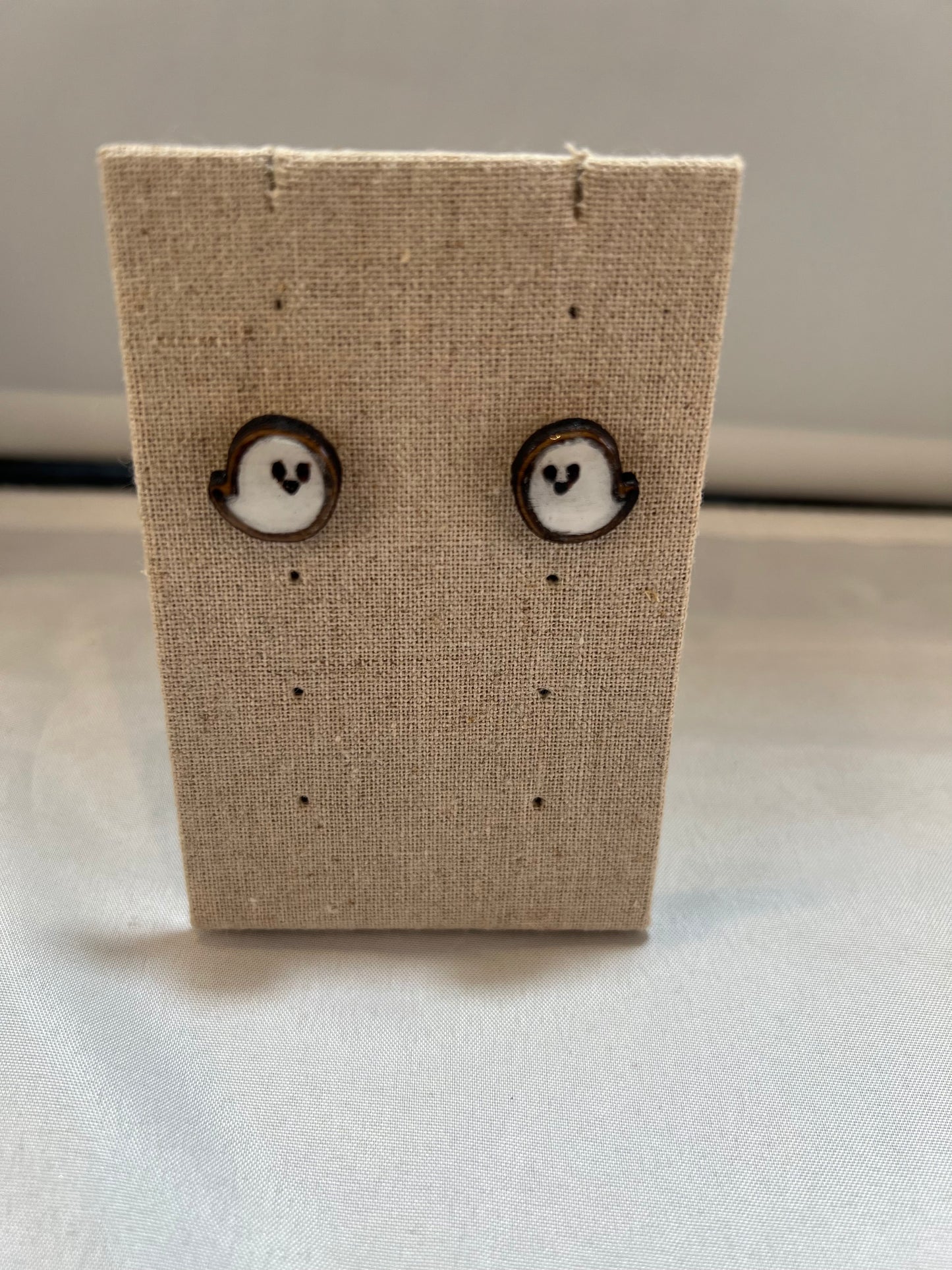 A pair of kawaii ghost earrings displayed on a beige cardboard backing, with a white and black color scheme.