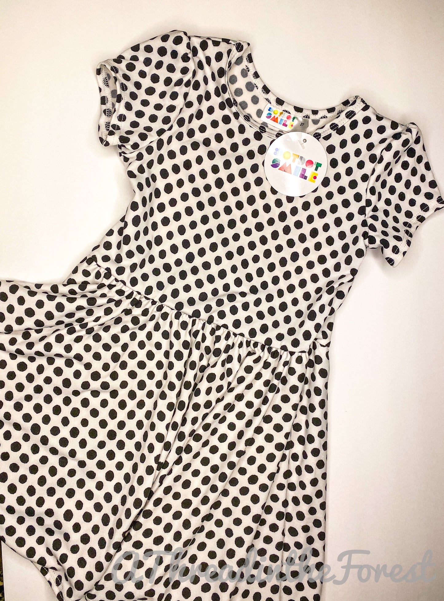 A white dress with black polka dots, displayed on a hanger, with a visible tag.