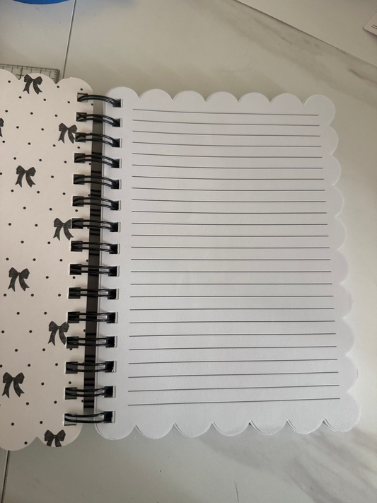 A spiral-bound notebook with a white lined page and a patterned cover featuring black birds and dots on a light background, photographed on a light marble-like surface.