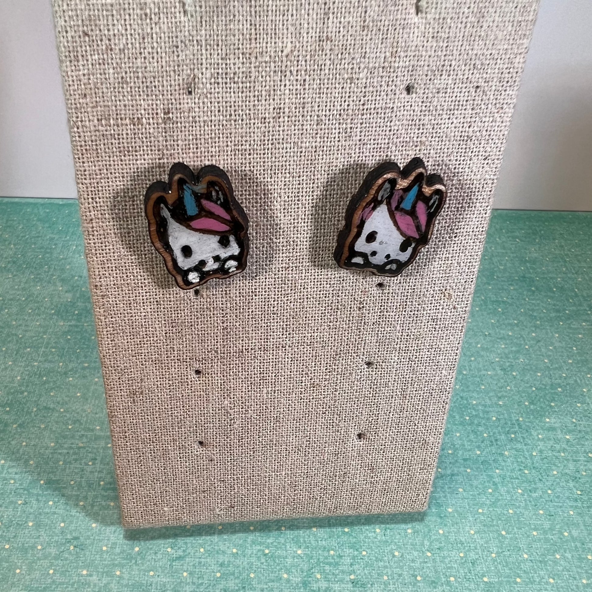 Pair of laser cut wood earrings, white unicorn faces with a pink mane and blue unicorn horns.
