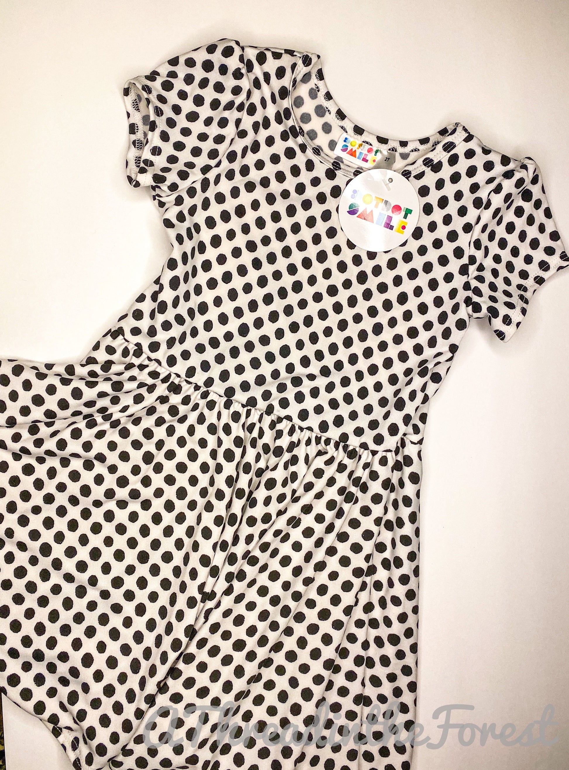 A white dress with black polka dots, displayed on a hanger, with a visible tag.