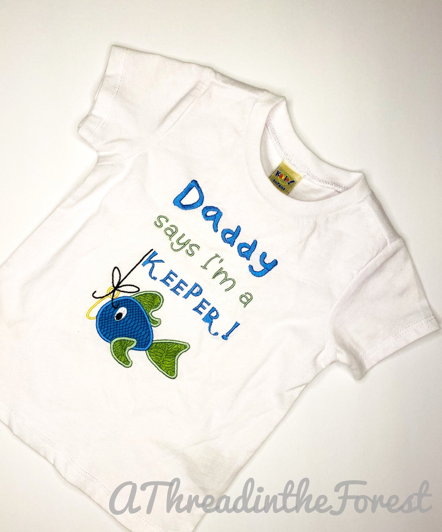 White embroidered shirt with blue and green fish with a hook. text says Daddy says I'm a Keeper
